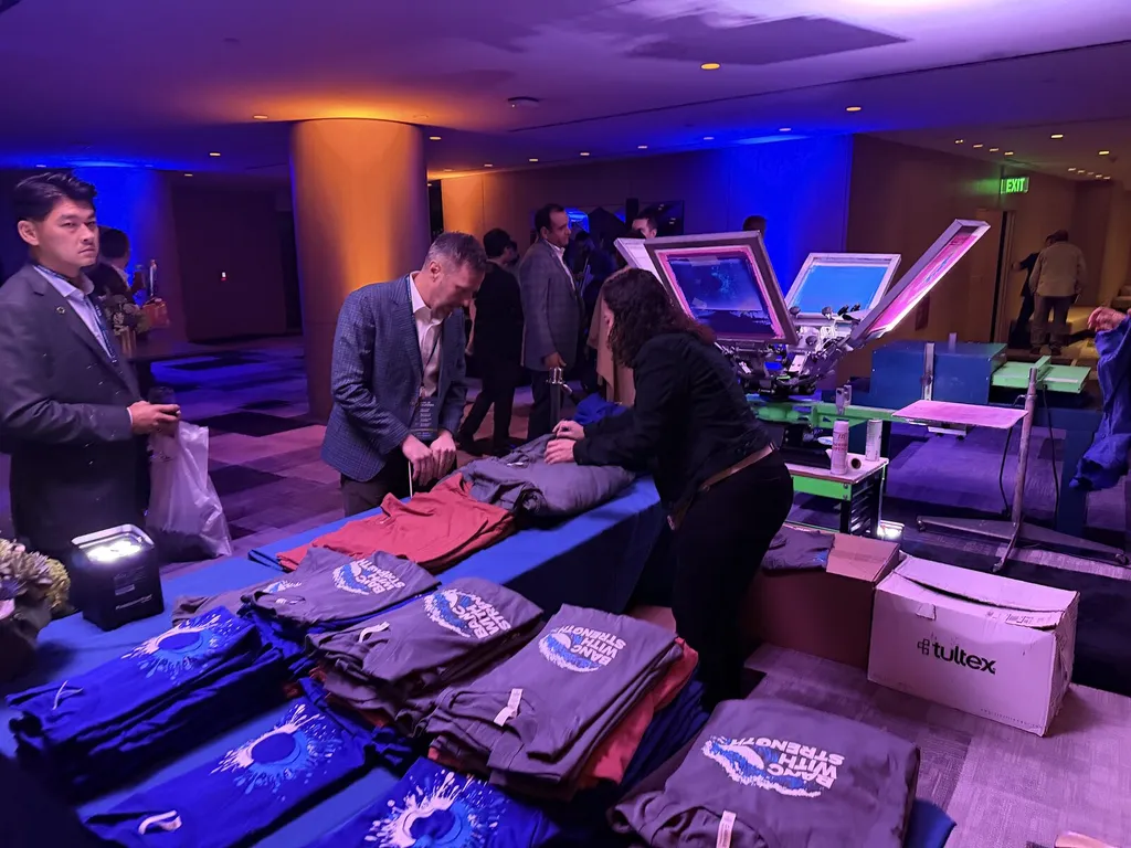 Guests in suits choosing shirts at a live screen printing station under blue event lighting