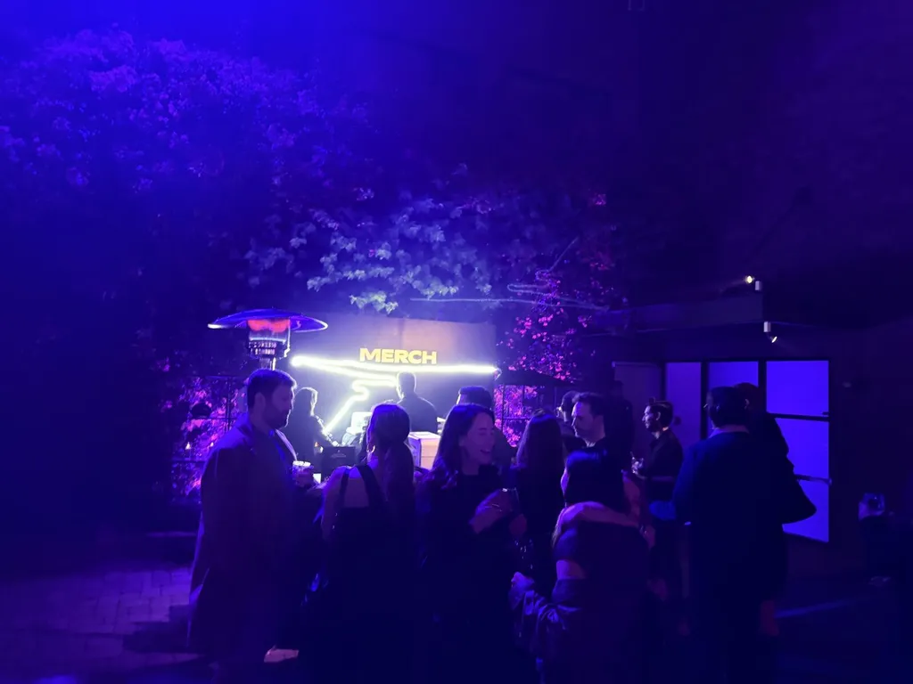 Neon Merch sign glowing over an outdoor evening event booth